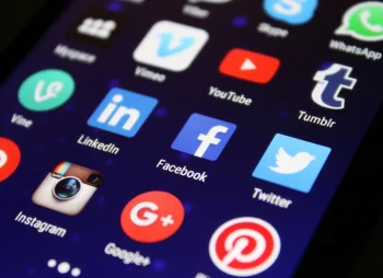 La imagen muestra una pantalla de teléfono móvil con íconos de aplicaciones brillantes sobre un fondo oscuro. Los íconos representan aplicaciones populares como WhatsApp, Vine, LinkedIn, YouTube, Tumblr, Facebook, Twitter, Instagram, Google+, y Pinterest. En cuanto a la relación con las empresas tech más famosas, estas aplicaciones están asociadas con algunas de las empresas tecnológicas más famosas del mundo, como Facebook, Google y Twitter