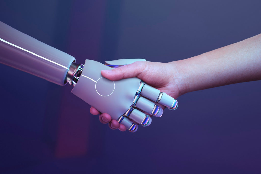 La imagen muestra un apretón de manos entre una mano humana y una mano robótica. Este apretón simboliza la integración de la tecnología en la educación.